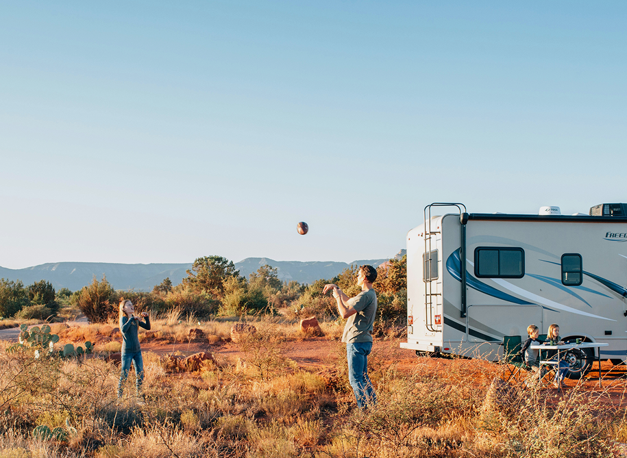 Family playing outside near a travel van on a sunny day